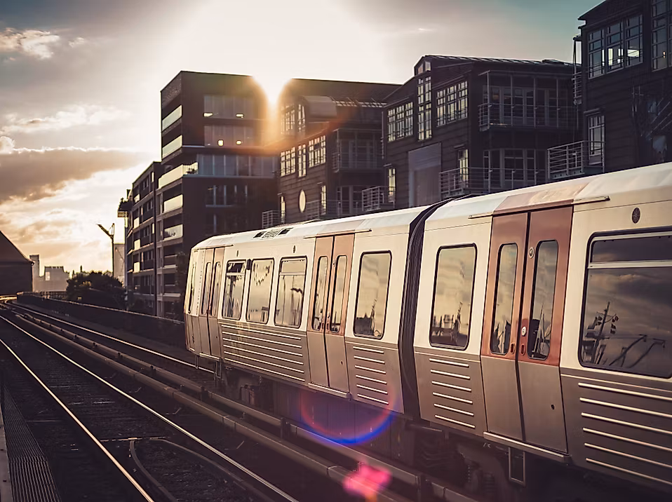 Hamburger U-Bahn fährt bei Sonnenuntergang auf Hochgleisen an modernen Wohnhäusern vorbei